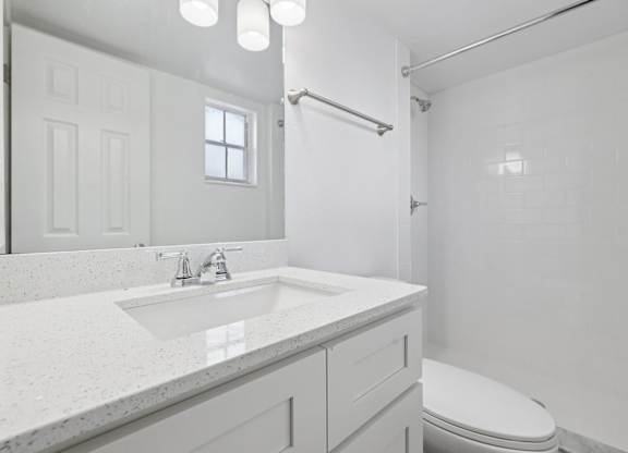 A white bathroom with a sink, toilet, and shower.