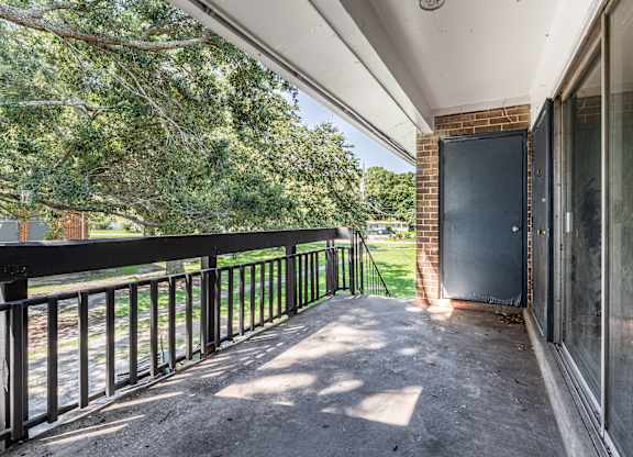 A balcony with a black railing and a view of trees and a brick building.
