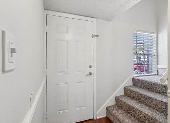 A white door is in a hallway with a staircase.