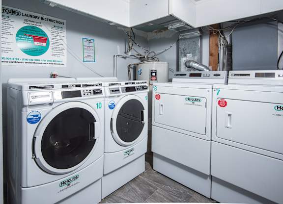 A row of white front load washing machines are lined up in a laundry room.