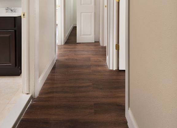 A long hallway with white doors and brown floors.