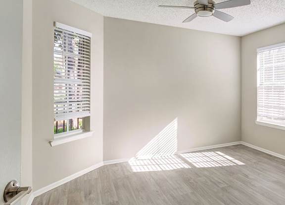 A room with a ceiling fan and two windows.