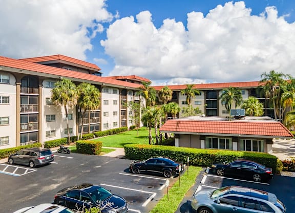 A parking lot with cars and a building with palm trees in front.
