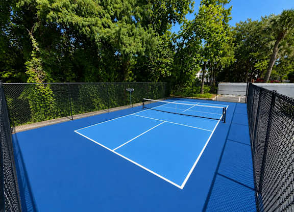 A blue pickleball court surrounded by a fence.