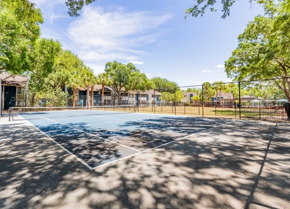 a tennis court with trees and a fence around it  at Fisherman's Landing Apartment Homes, Tampa, Florida