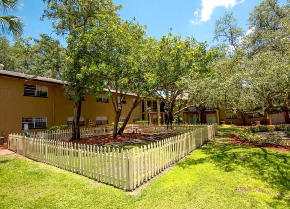 a yard with a fence and trees in front of a yellow house  at Oak Manor Apartment Homes, Tampa