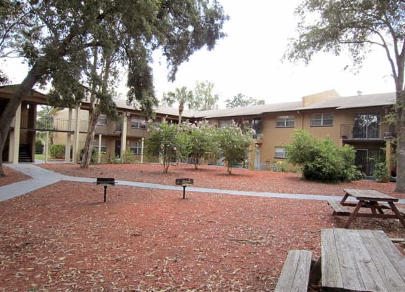 a courtyard with picnic tables and benches in front of an apartment building  at Oak Manor Apartment Homes, Tampa, FL, 33617