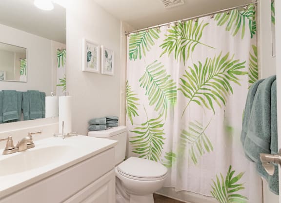 A bathroom with a white sink, toilet, and a green leafy shower curtain.
