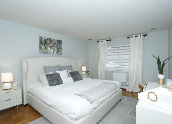 A white bedroom with a large bed and a nightstand with a plant on it.