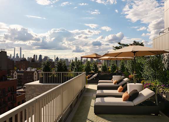 A rooftop patio with lounge chairs and umbrellas overlooking a city skyline.