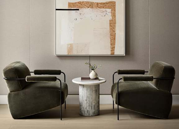 Two chairs and a table are in front of a framed artwork.