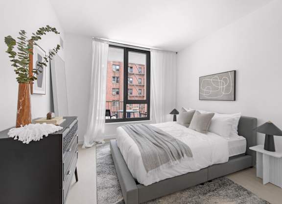A bedroom with a large bed, a dresser, and a window with a view of a building outside.