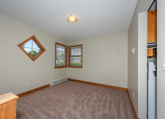 an empty living room with two windows and a kitchenette
