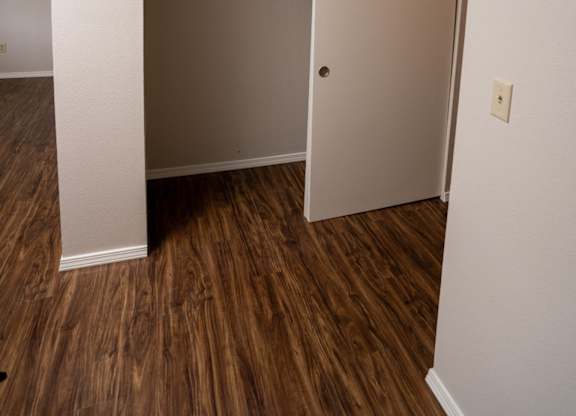 A white door is open to a room with wood flooring.