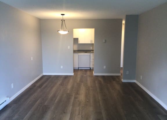 an empty living room with a kitchen in the background