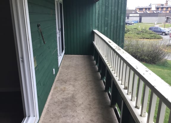 a balcony with a concrete floor and a green building in the background