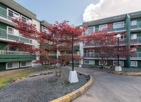 a view of the entrance to a green apartment building with red trees in front of it