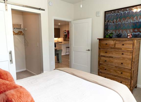 A bedroom with a large bed, a wooden dresser, and a painting on the wall.