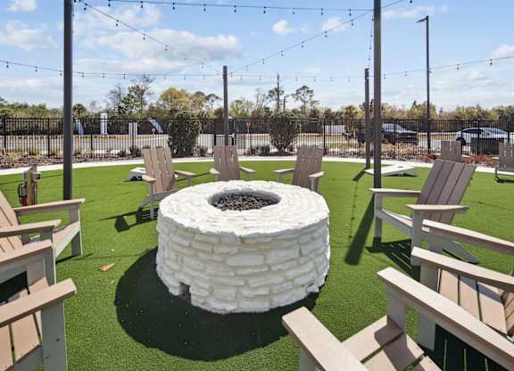 A white fire pit sits in the middle of a grassy area surrounded by wooden chairs. at Allegra at Cocoa in Cocoa, FL, 32926