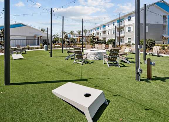 Cornhole and firepit seating on turf with string lights above at Allegra at Cocoa in Cocoa, FL, 32926
