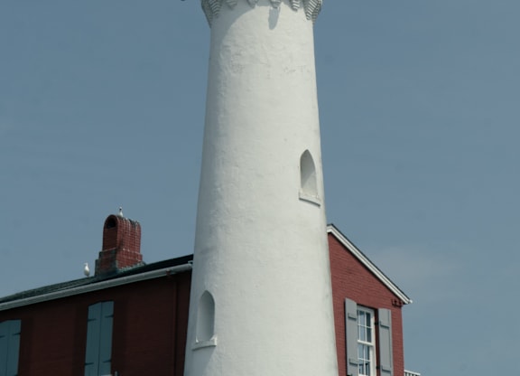 A white lighthouse with a red roof stands tall against a blue sky.