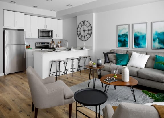 a living room with a kitchen in the background and a couch and chairs in the foreground