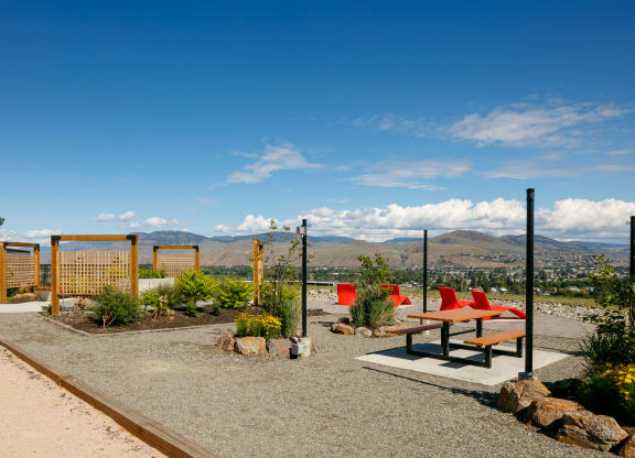 a picnic table and benches sit in a gravel area with a view of the mountains in the