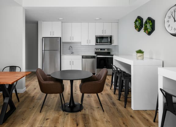 a room with a table and chairs and a kitchen in the background