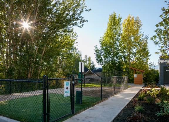 a fenced in dog park with a house and trees in the background