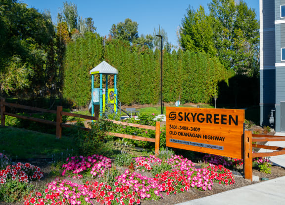 a garden with pink and purple flowers and a blue playground in the background