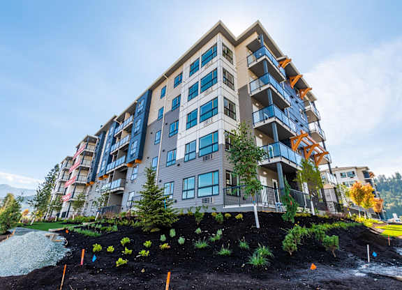 A modern multi-story building with balconies and a landscaped area in front.