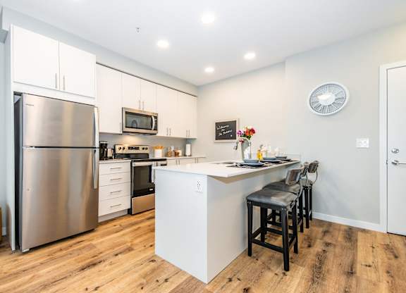 A modern kitchen with a stainless steel refrigerator and a white island with bar stools.