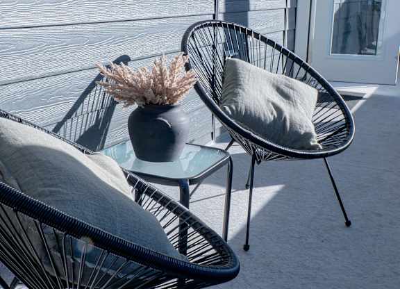 Two black wicker chairs with grey cushions are placed on a patio.