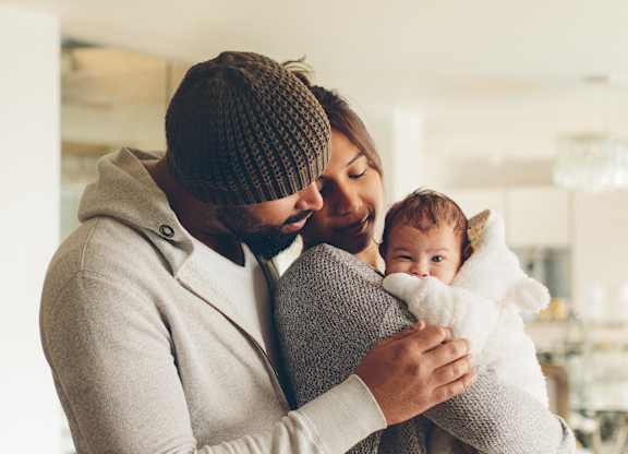 A man in a beanie and a woman in a striped sweater are holding a baby.