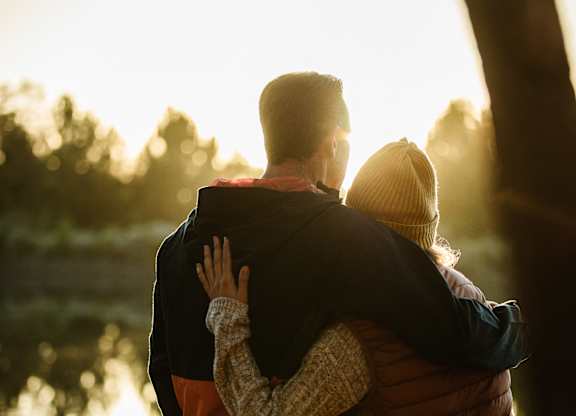 A couple is hugging each other in a sunny outdoor setting.