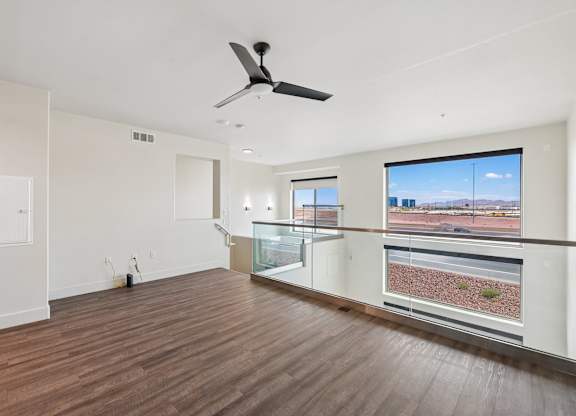 A room with a ceiling fan and a balcony with a view of the outside.