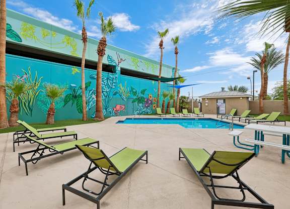A pool area with green lounge chairs and a mural of palm trees.