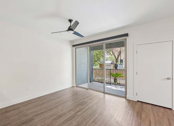A room with a ceiling fan and sliding glass doors leading to a balcony.