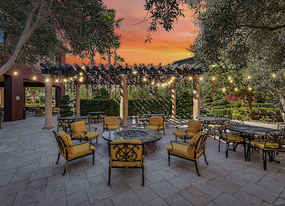 A patio with tables and chairs is set up under a canopy with lights strung up.