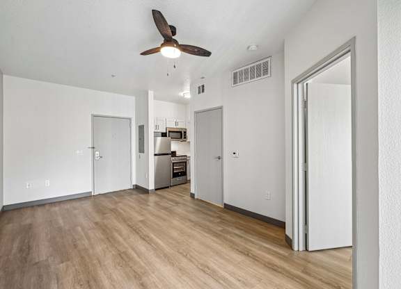A room with a ceiling fan and a kitchen area in the background.