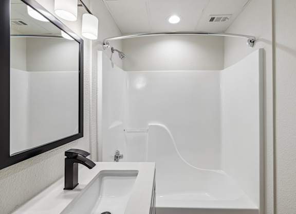 A white bathroom with a sink, mirror, and bathtub.