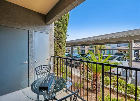 A balcony with a glass table and chairs overlooking a street.