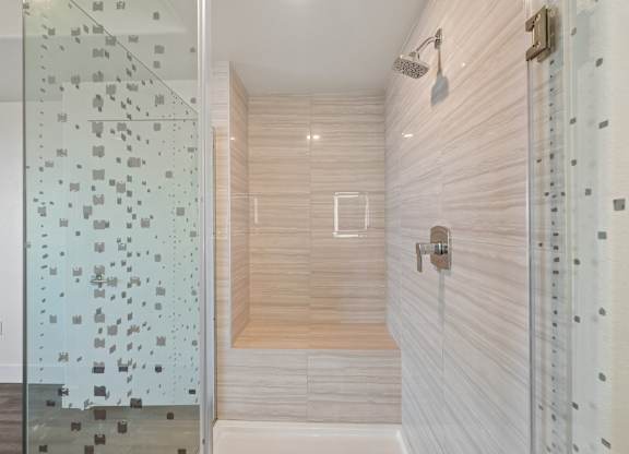 A modern bathroom with a glass shower enclosure and a wooden floor.