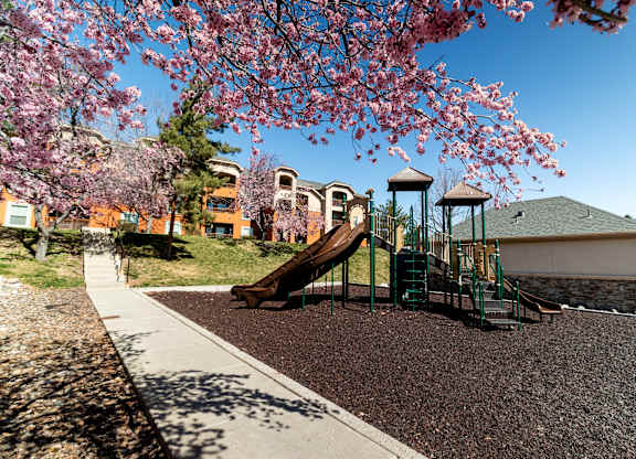 A playground with a slide and a tree with pink flowers.