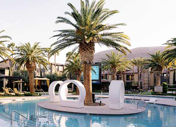 A pool surrounded by palm trees and lounge chairs.