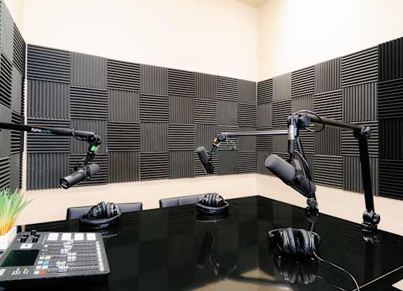 A black desk with a soundproof booth and microphones.