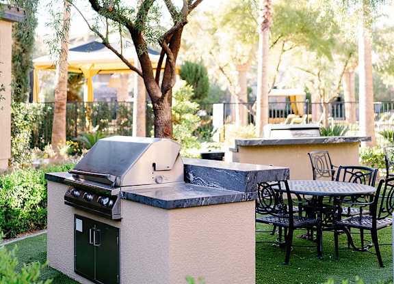 A large tree in a yard with a grill and table.