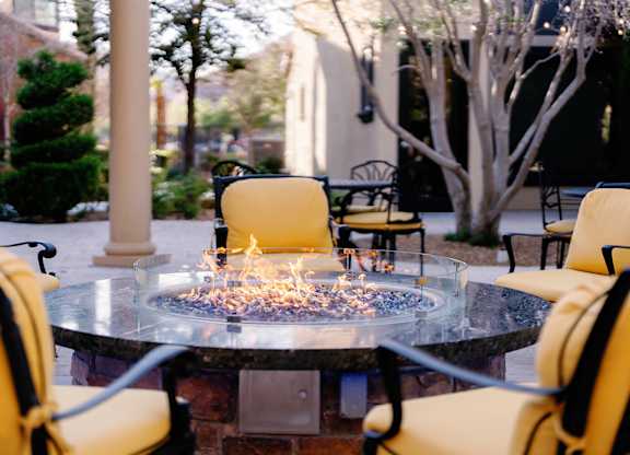 A fire pit in the middle of a patio surrounded by yellow chairs.