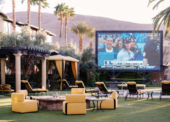A large screen is set up in a backyard with a pool and lounge chairs.