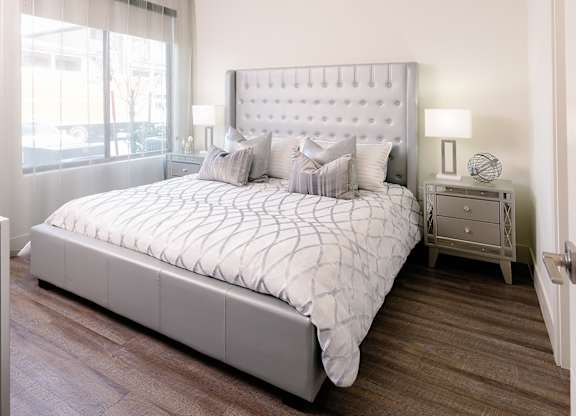 A bed with a white headboard and pillows is in a room with wooden flooring.